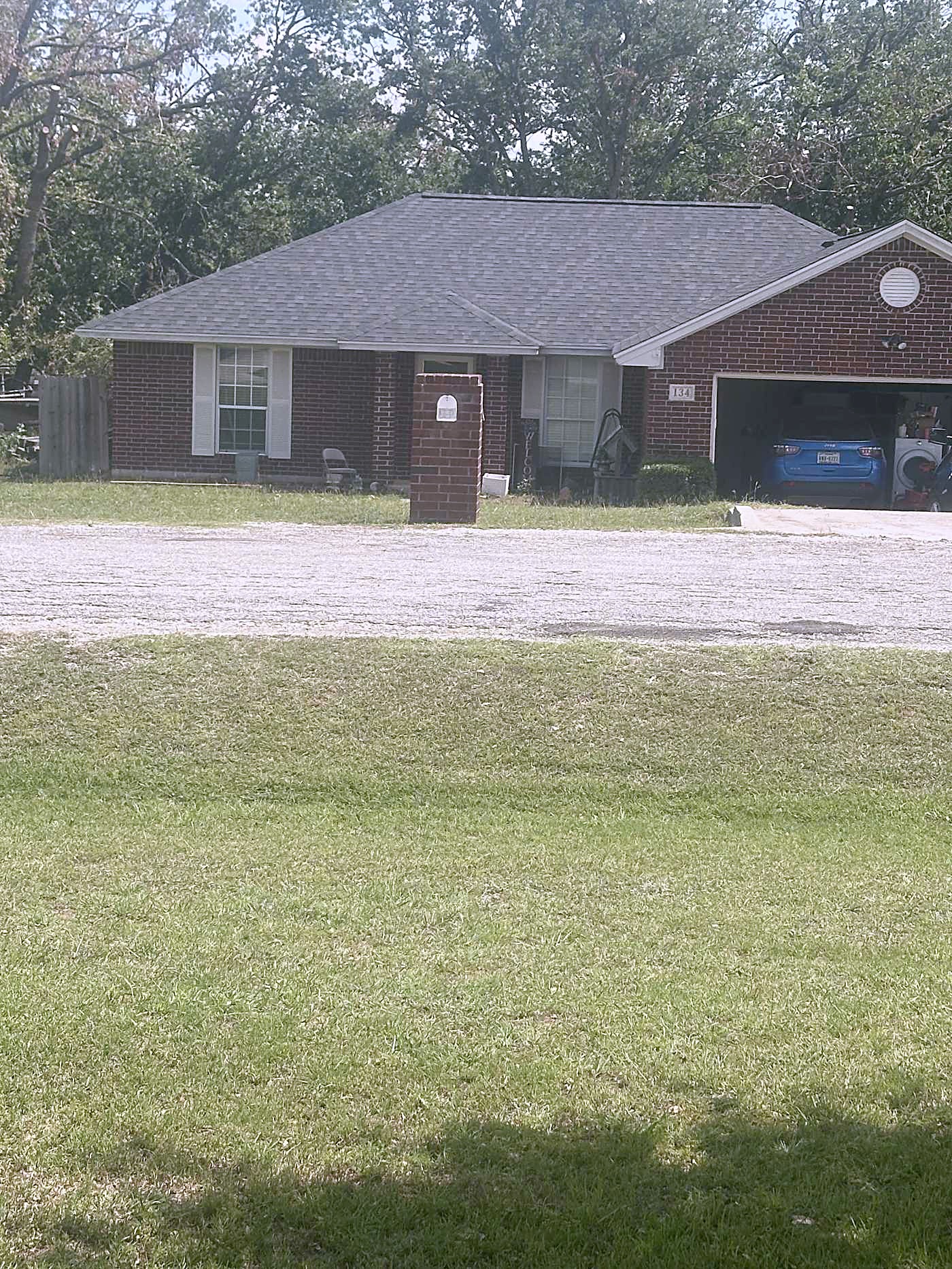A single story brick home with a gray shingle roof seen across a lawn