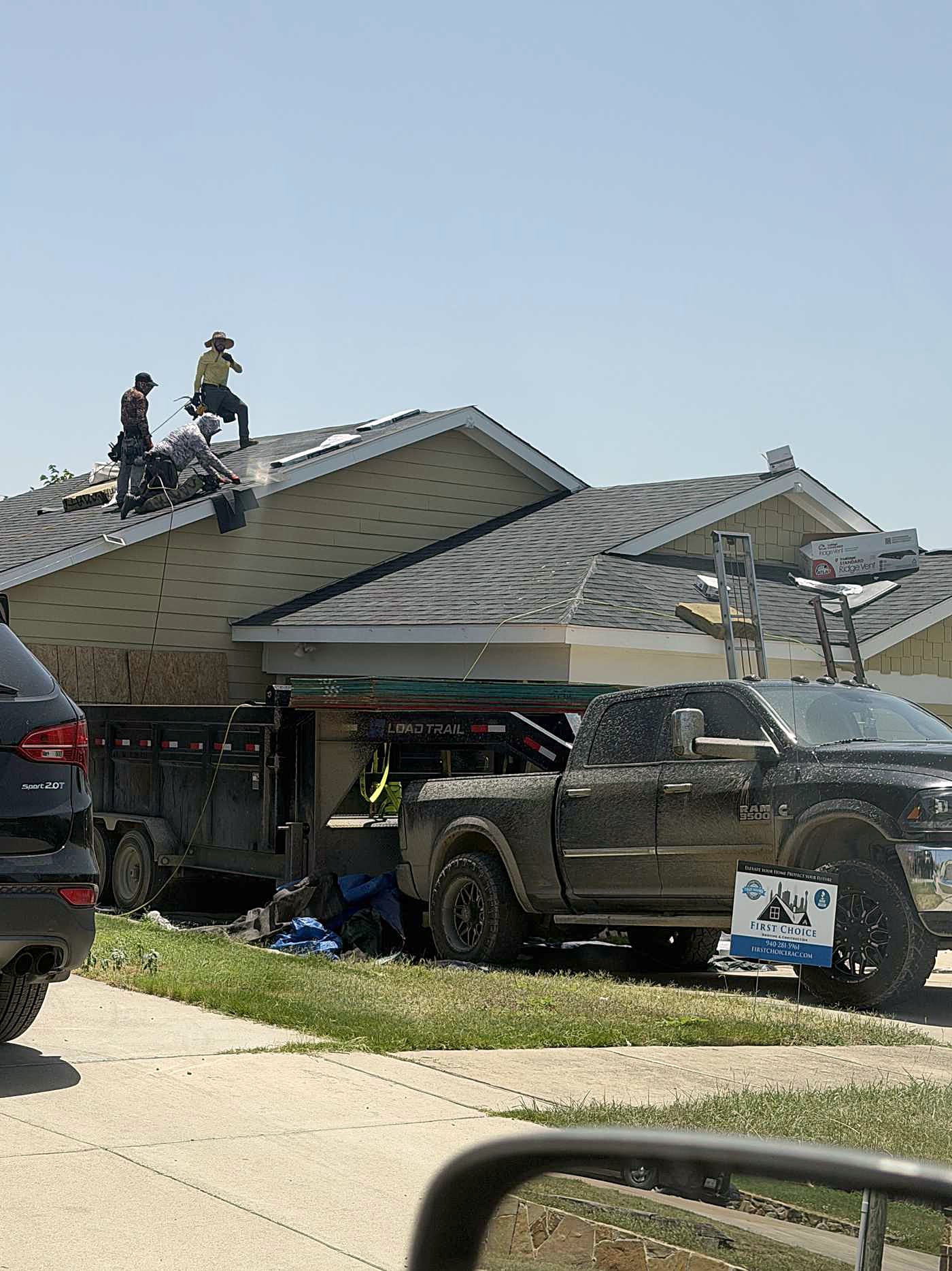 Roofers working on a roof with a dump trailer and pickup truck in the driveway