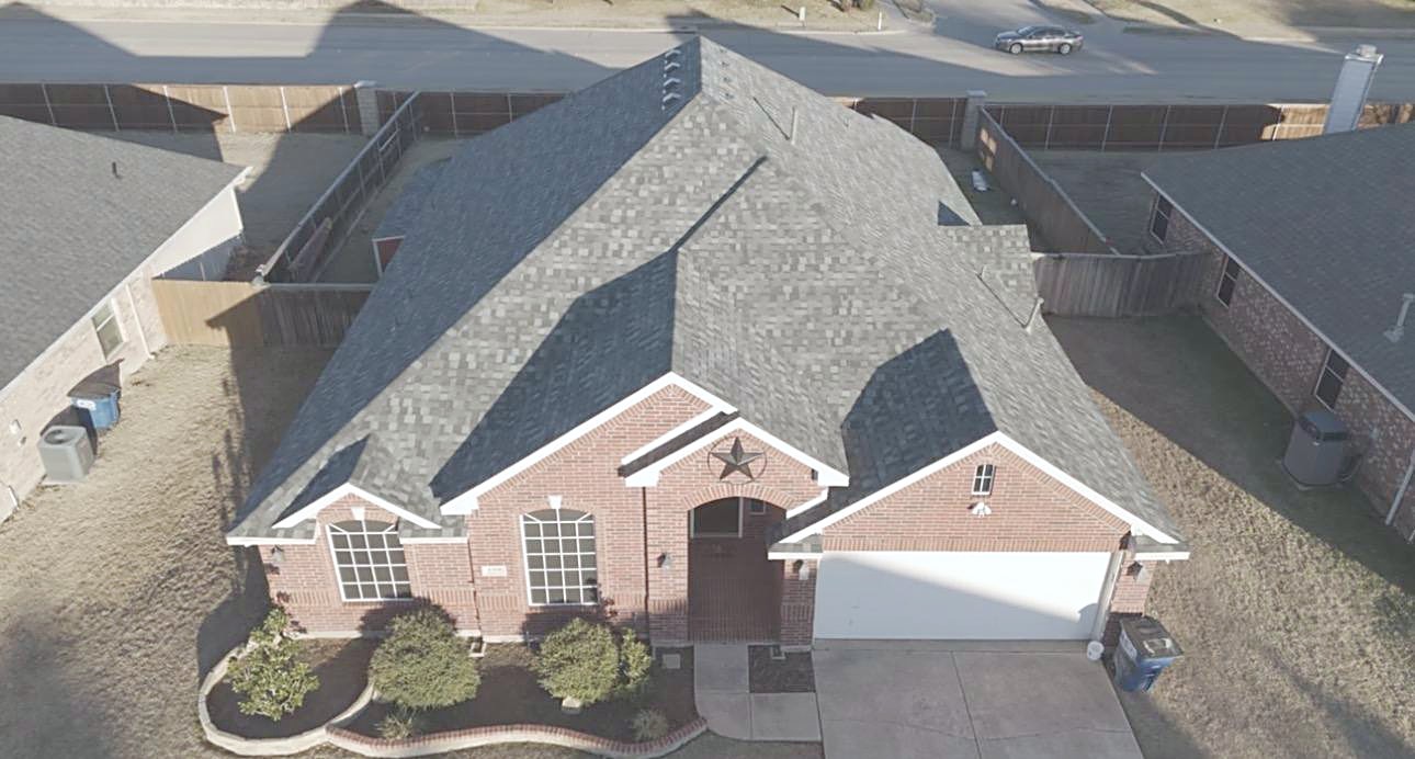 Drone view of a brick home with a star on the gable and a gray shingle roof in low sun