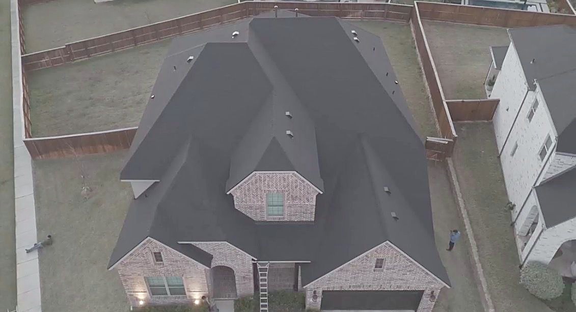 Overhead drone view of a two story brick home with a finished charcoal roof