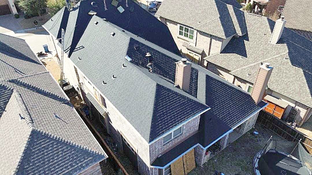 Drone view of two story homes with dark shingle roofs in a neighborhood