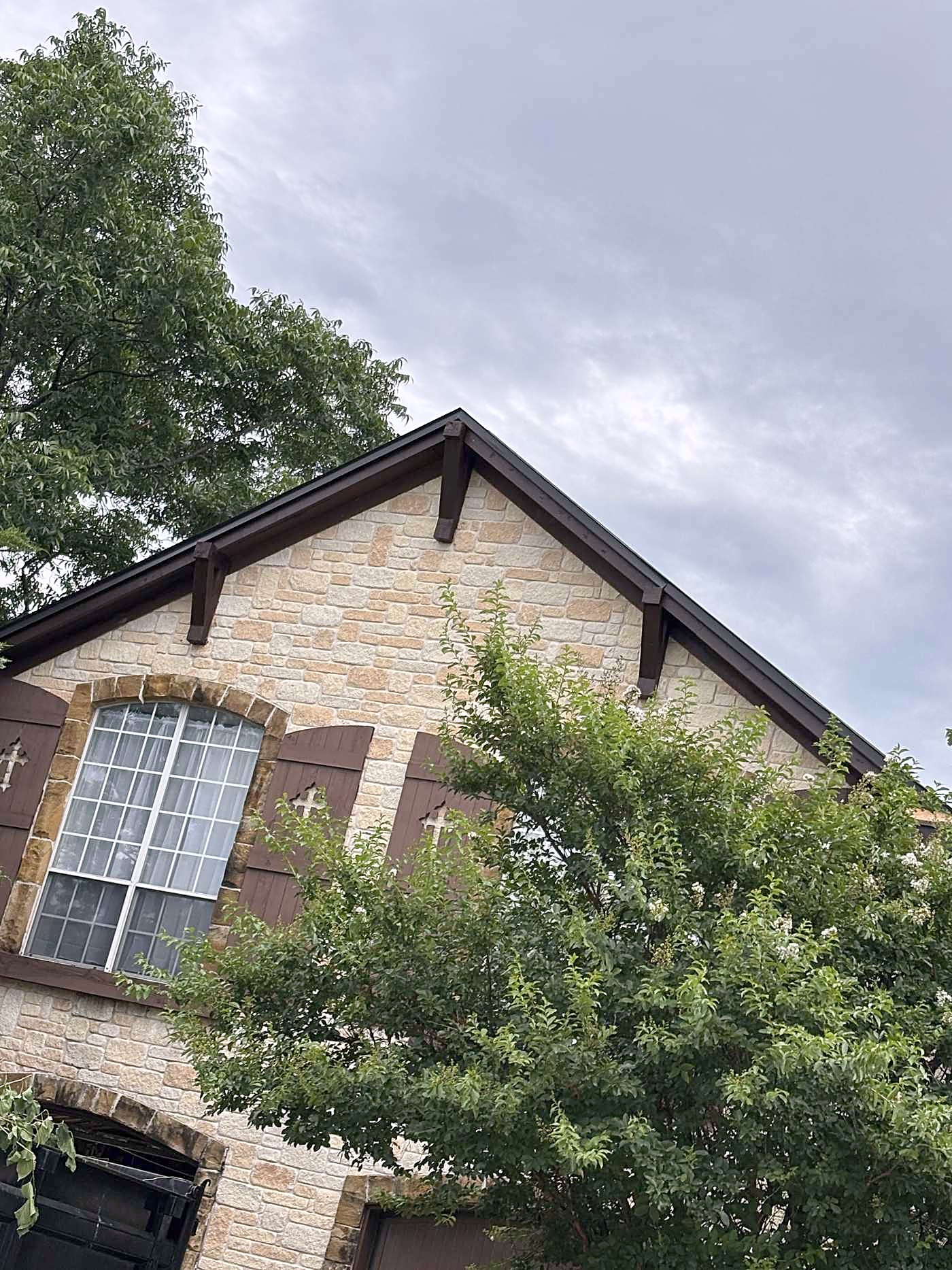 A stone front gable with dark trim and a gutter under a cloudy sky