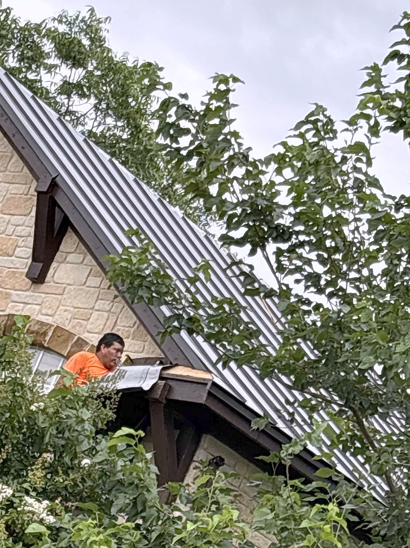 A worker fitting a gutter beside a dark metal roof section